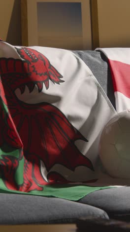 Vertical-Video-Of-Sofa-In-Lounge-With-English-And-Welsh-Flags-And-Ball-As-Fans-Prepare-To-Watch-Football-Soccer-Match-On-TV